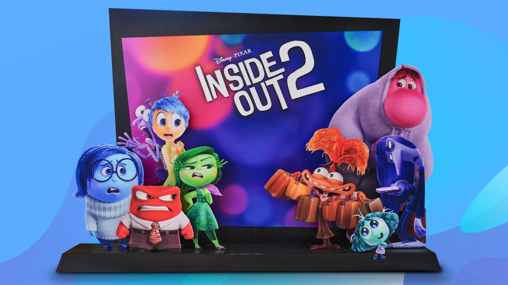 A screen says ‘Inside Out 2’ and it shows the Emotion characters from the Pixar movie, and it’s all on a blue-purple background. 